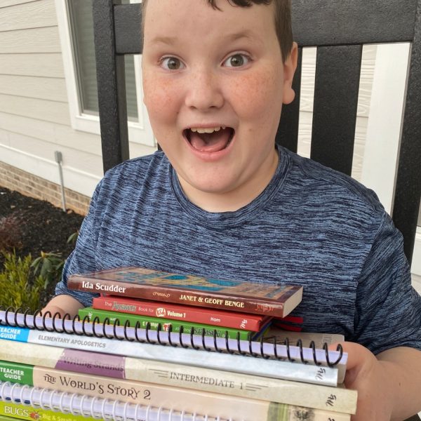 Excited boy holding a stack of homeschool curriculum including elementary apologetics and history books